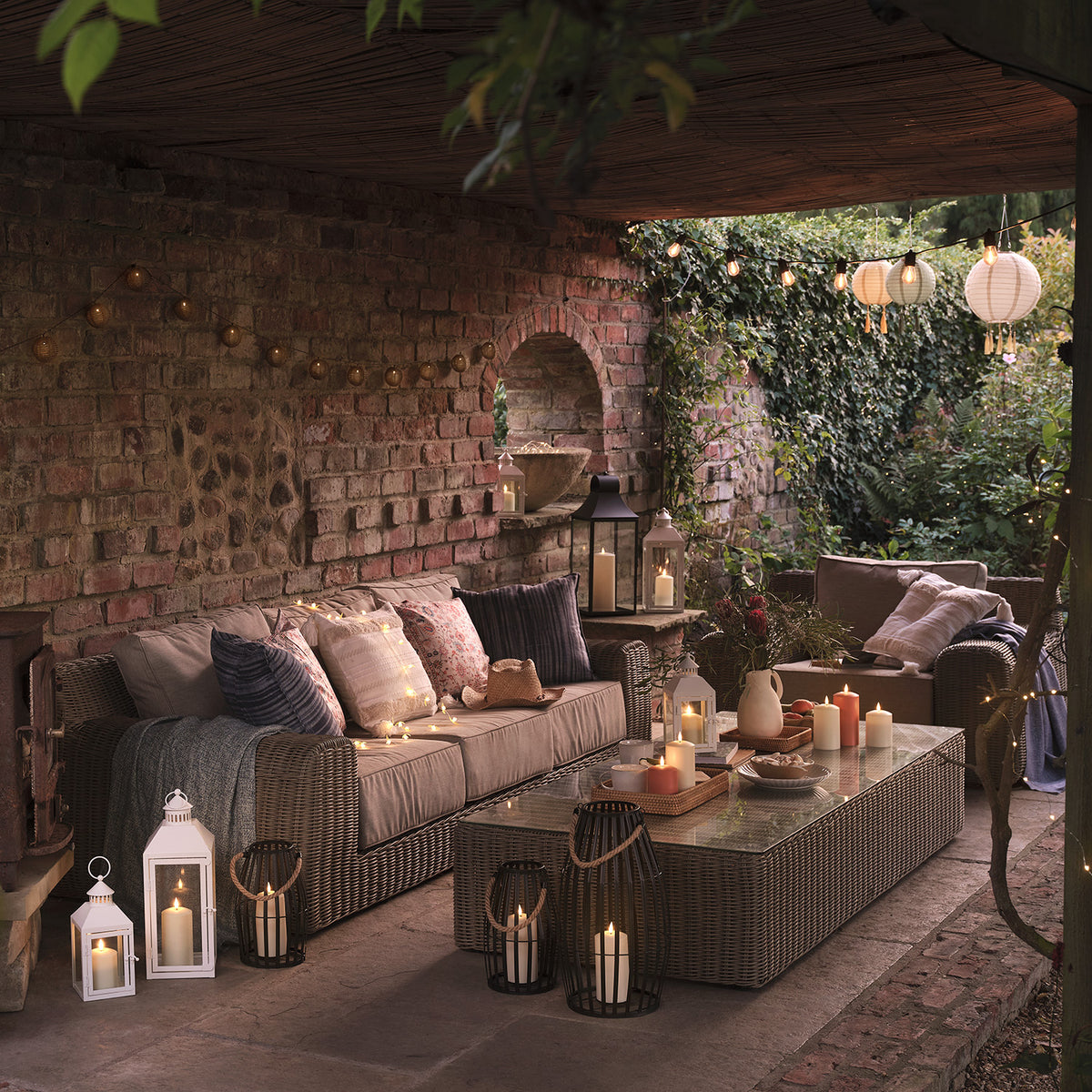 Überdachte Terrasse mit Sofa, Tisch, Laternen und Kerzen in gemütlicher Abendstimmung