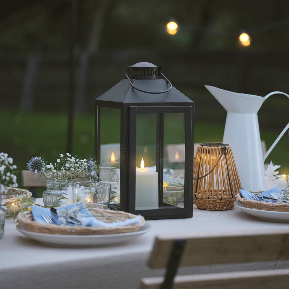 Schwarze LED-Laterne mit TruGlow Kerze auf gedecktem Gartentisch bei Abendlicht