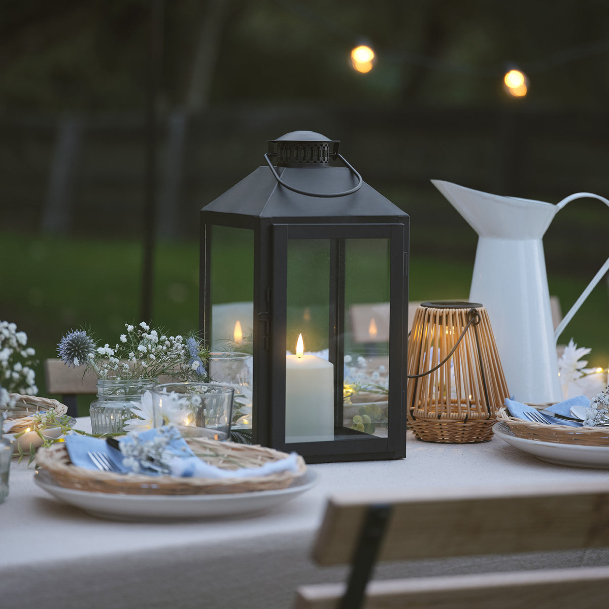 Schwarze LED-Laterne mit TruGlow Kerze auf gedecktem Gartentisch bei Abendlicht