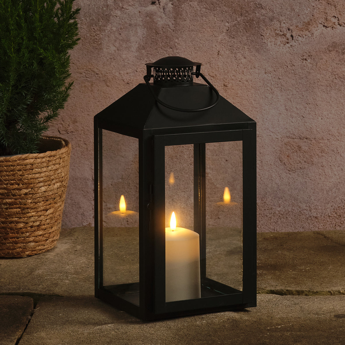 Große schwarze Laterne mit TruGlow LED-Kerze neben Pflanze auf Steinboden