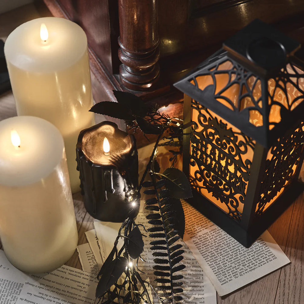 Halloween-Laterne mit Flammeneffekt neben weißen und schwarzer Kerze auf alten Buchseiten
