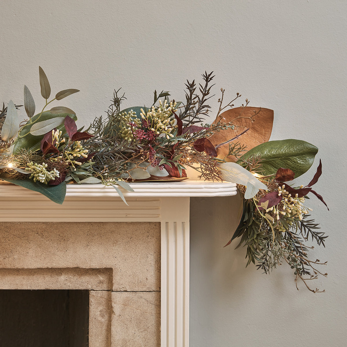 Herbstliche Girlande mit grünen, orangefarbenen und roten Blättern auf Kaminsims mit warmweißen LEDs