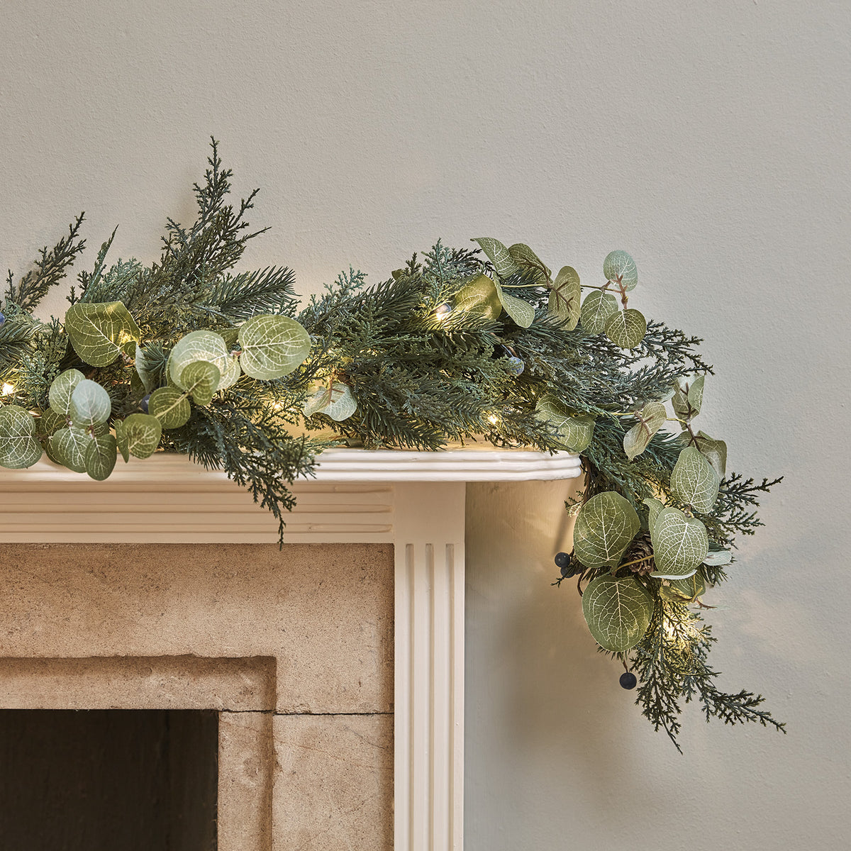 Beleuchtete Weihnachtsgirlande mit Beeren, Tannenzapfen und Eukalyptus auf Kaminsims drapiert