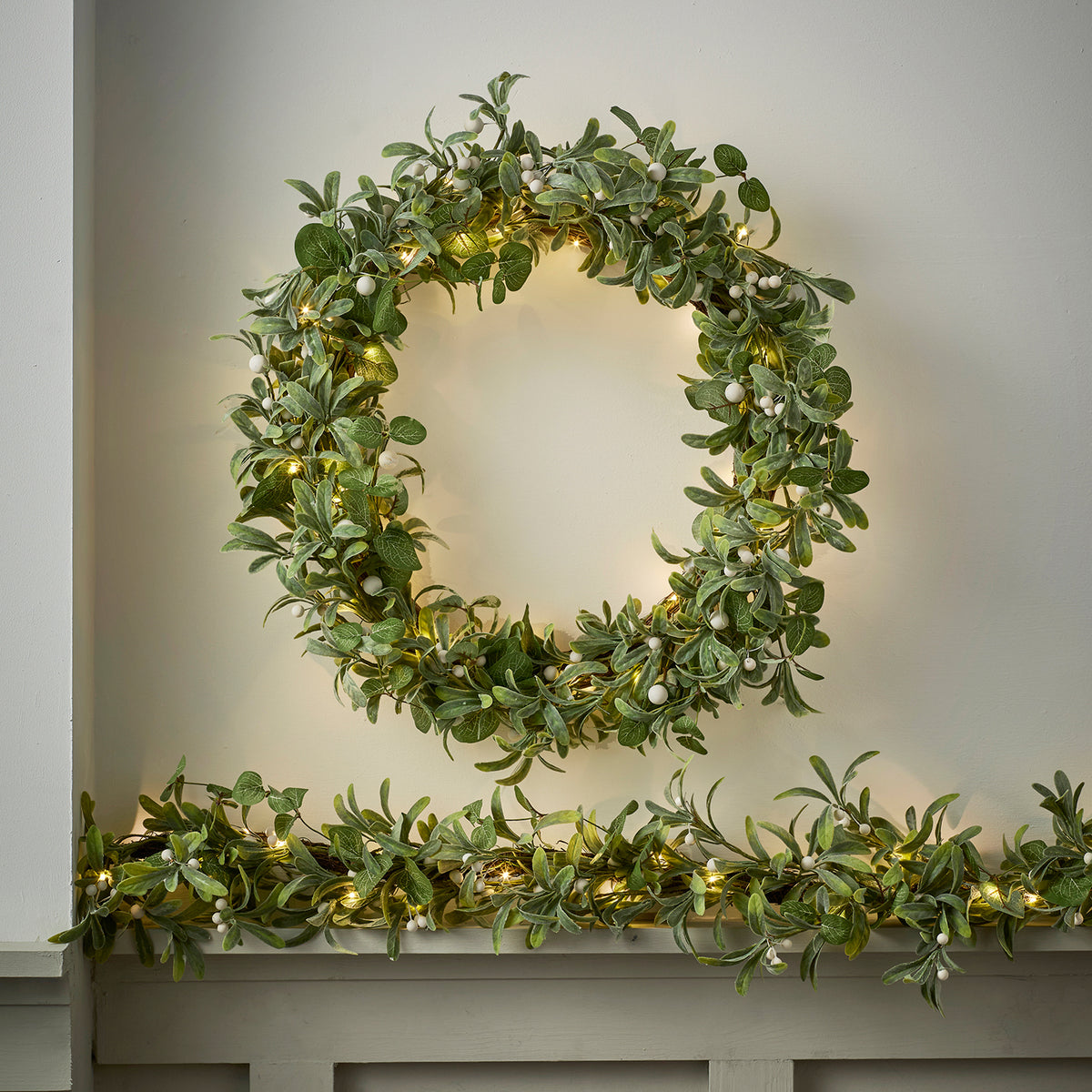 Weihnachtskranz aus Mistelzweigen und Eukalyptus mit weißen Beeren und warmweißen Lichtern an Wand