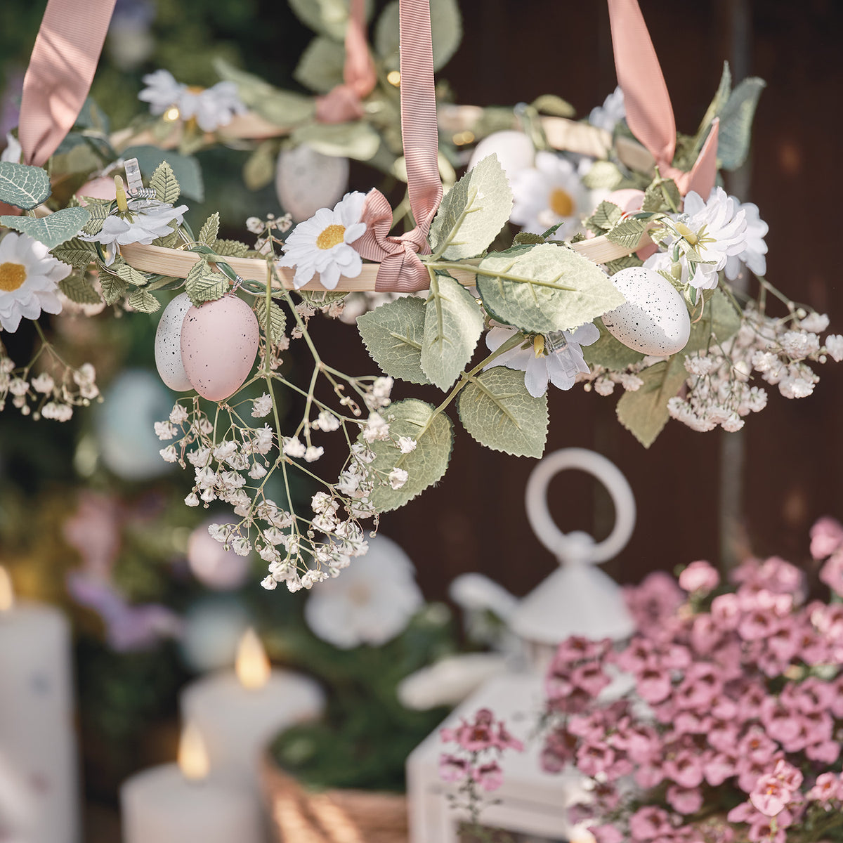 Ostereier und Gänseblümchen an Girlande mit LED-Lichtern, dekorativ aufgehängt mit rosa Bändern
