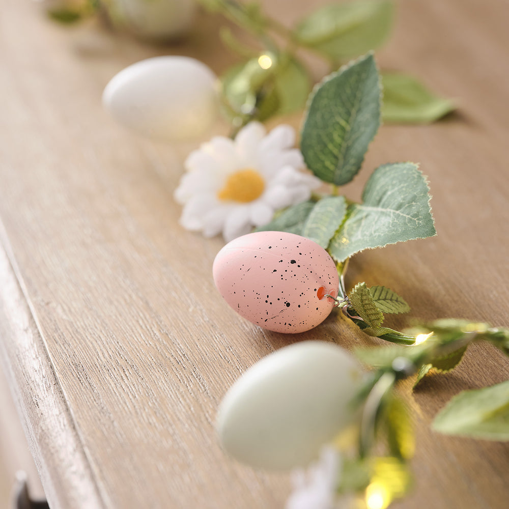 Nahaufnahme der Girlande mit rosa und weißen Ostereiern, grünen Blättern und Gänseblümchen