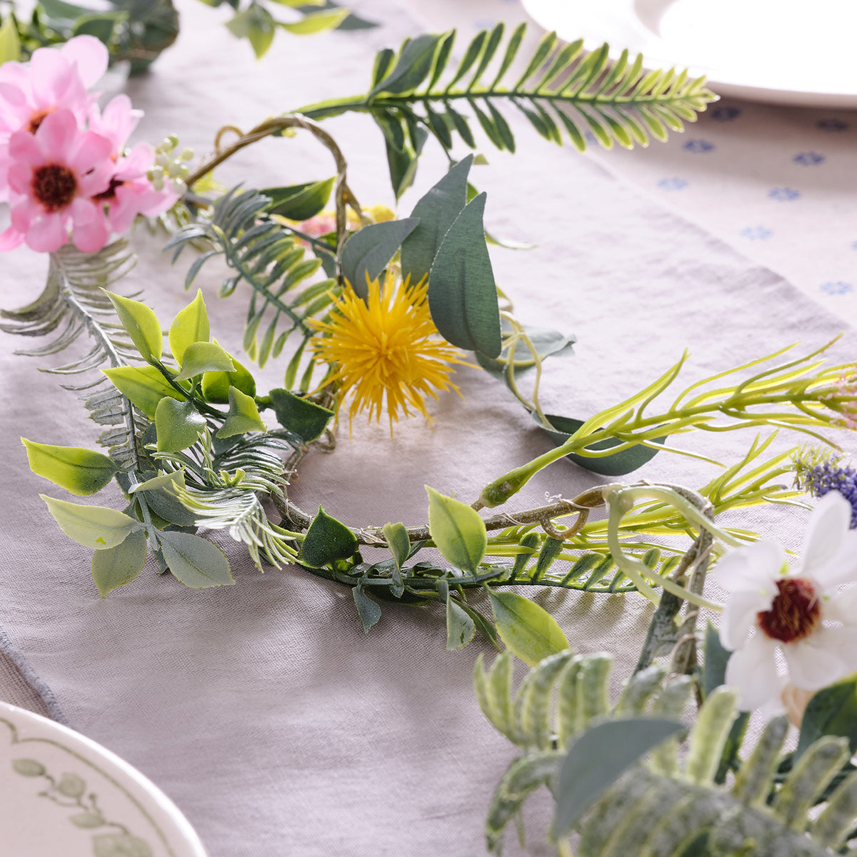 Frühlingsgirlande mit grünen Blättern und bunten Blumen auf einem hellen Tischtuch mit warmweißen LEDs