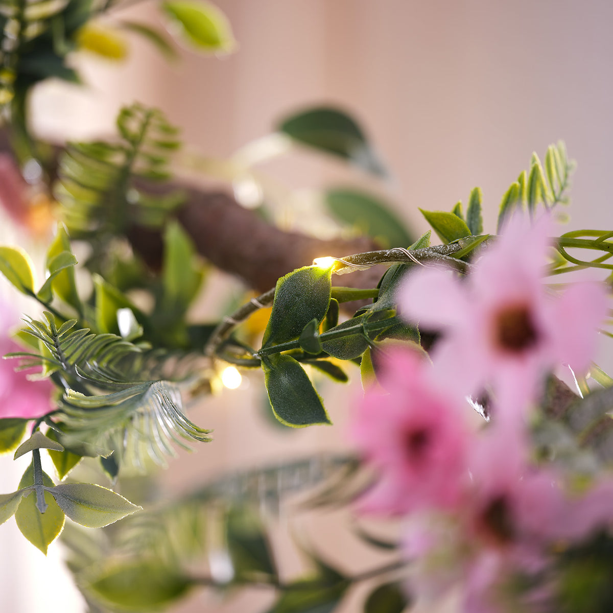 Nahaufnahme einer Frühlingsgirlande mit grünen Blättern, rosa Blüten und warmweißen LED-Lichtern