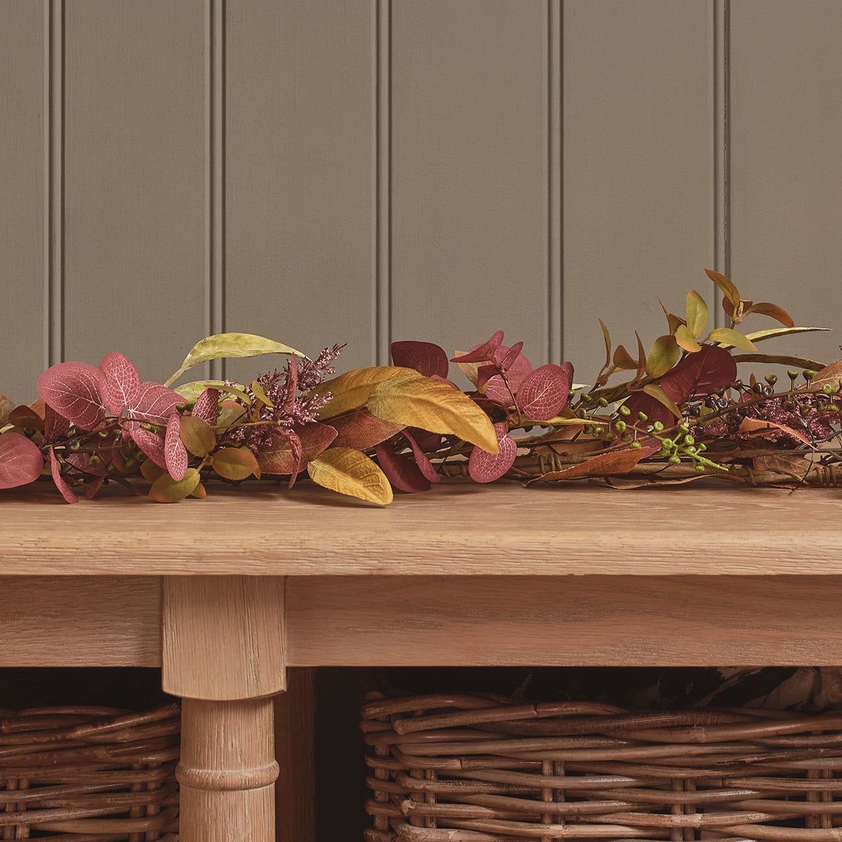 Nahaufnahme der Herbstgirlande mit warmweißen LEDs und buntem Laub auf einem Holztisch