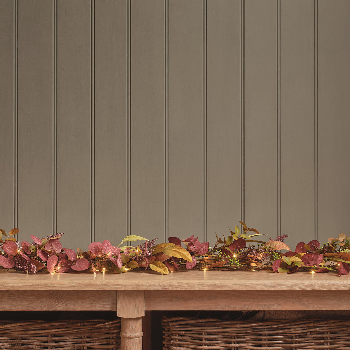 Herbstgirlande mit buntem Laub in Rot- und Grüntönen auf Holztisch vor brauner Wand