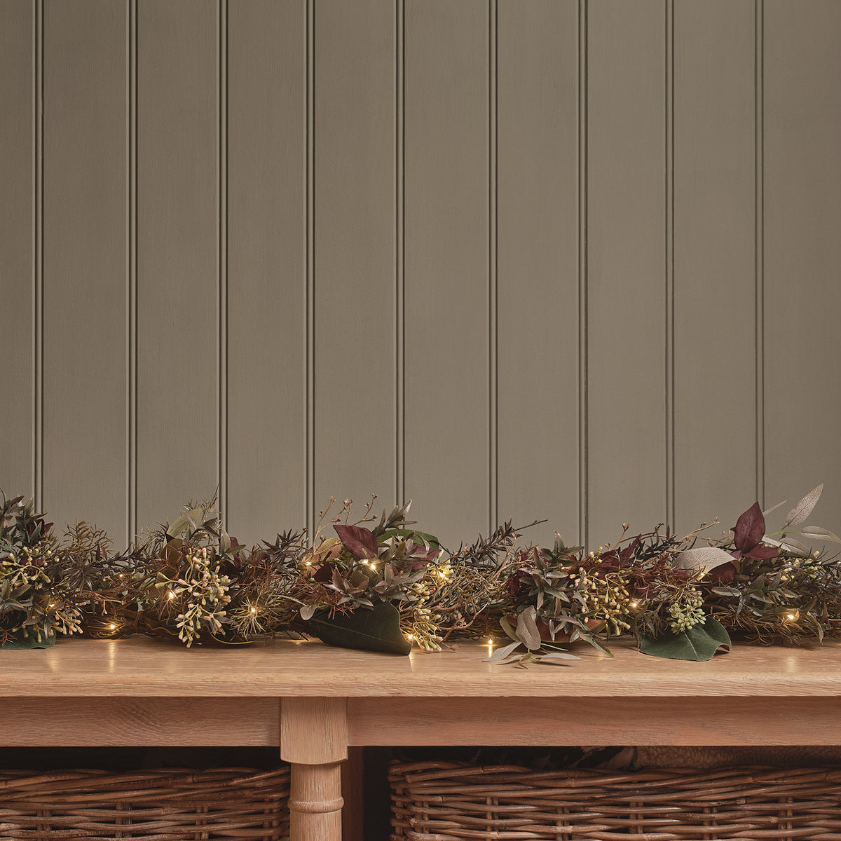 Herbstgirlande mit warmweißen Lichtern dekorativ auf einem Holztisch vor grauer Wand
