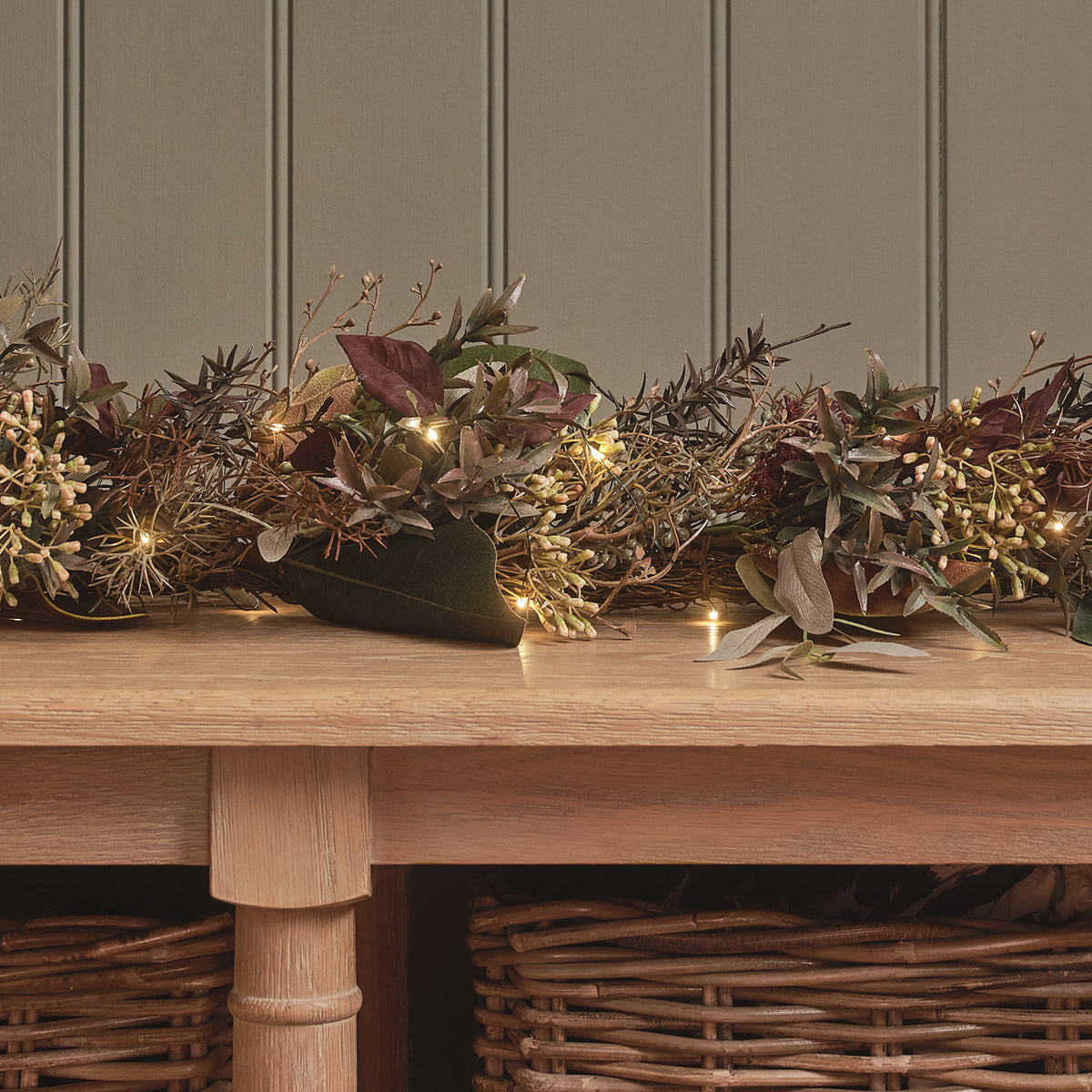 Herbstliche Girlande mit warmweißen LED-Lichtern und buntem Laub auf Holztisch
