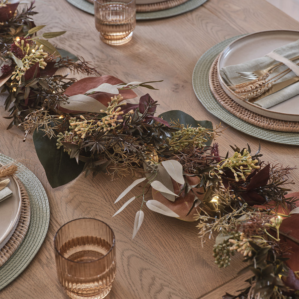Herbstliche Girlande mit buntem Laub und warmweißen LEDs auf einem gedeckten Holztisch