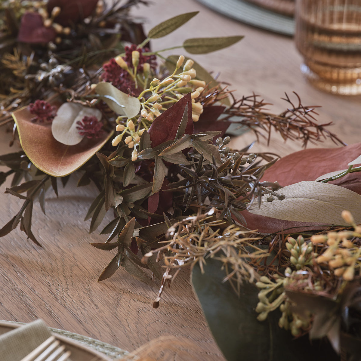 Herbstgirlande mit warmweißen LEDs und buntem Laub auf einem gedeckten Holztisch