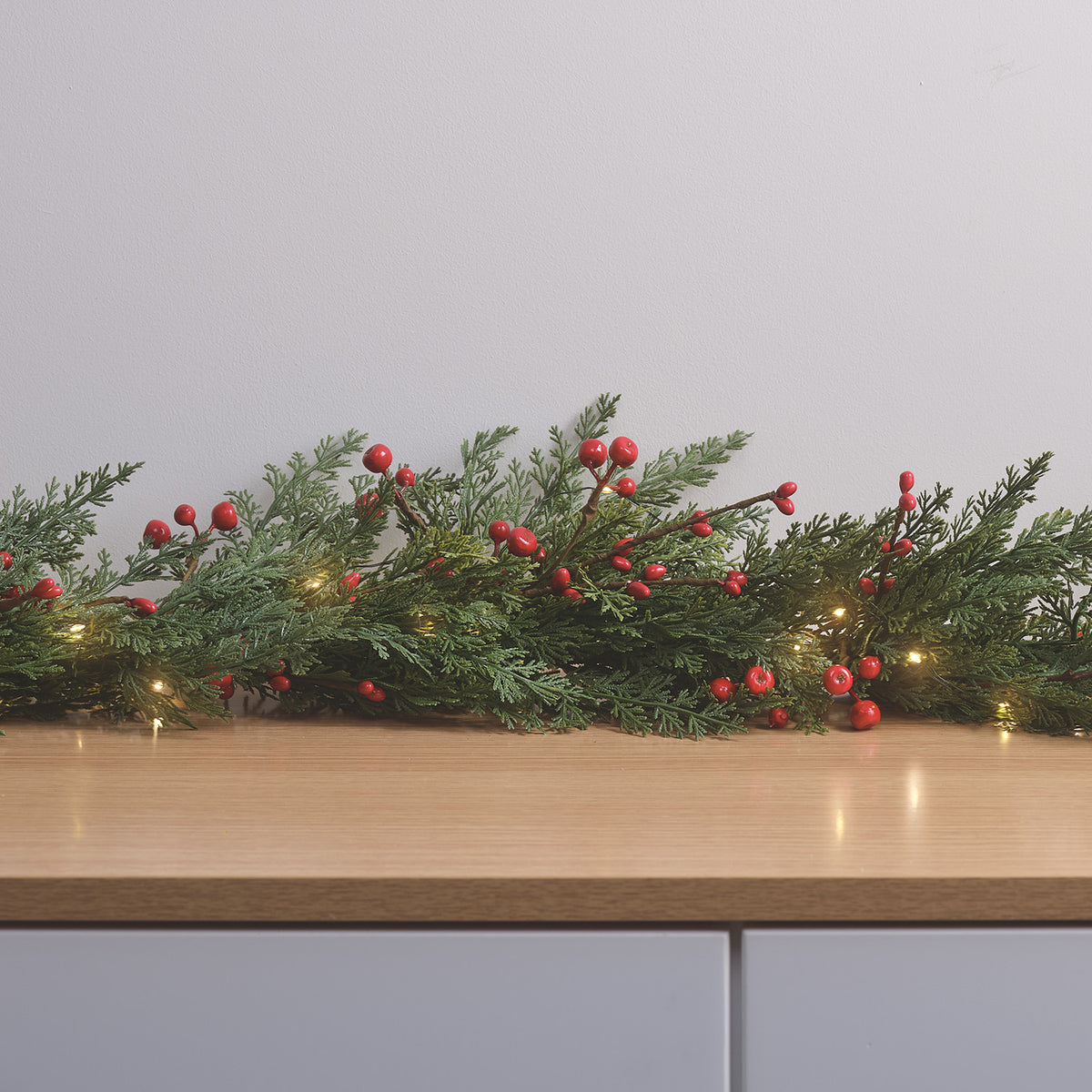 Weihnachtsgirlande mit roten Beeren und warmweißen LEDs dekorativ auf Holztisch drapiert