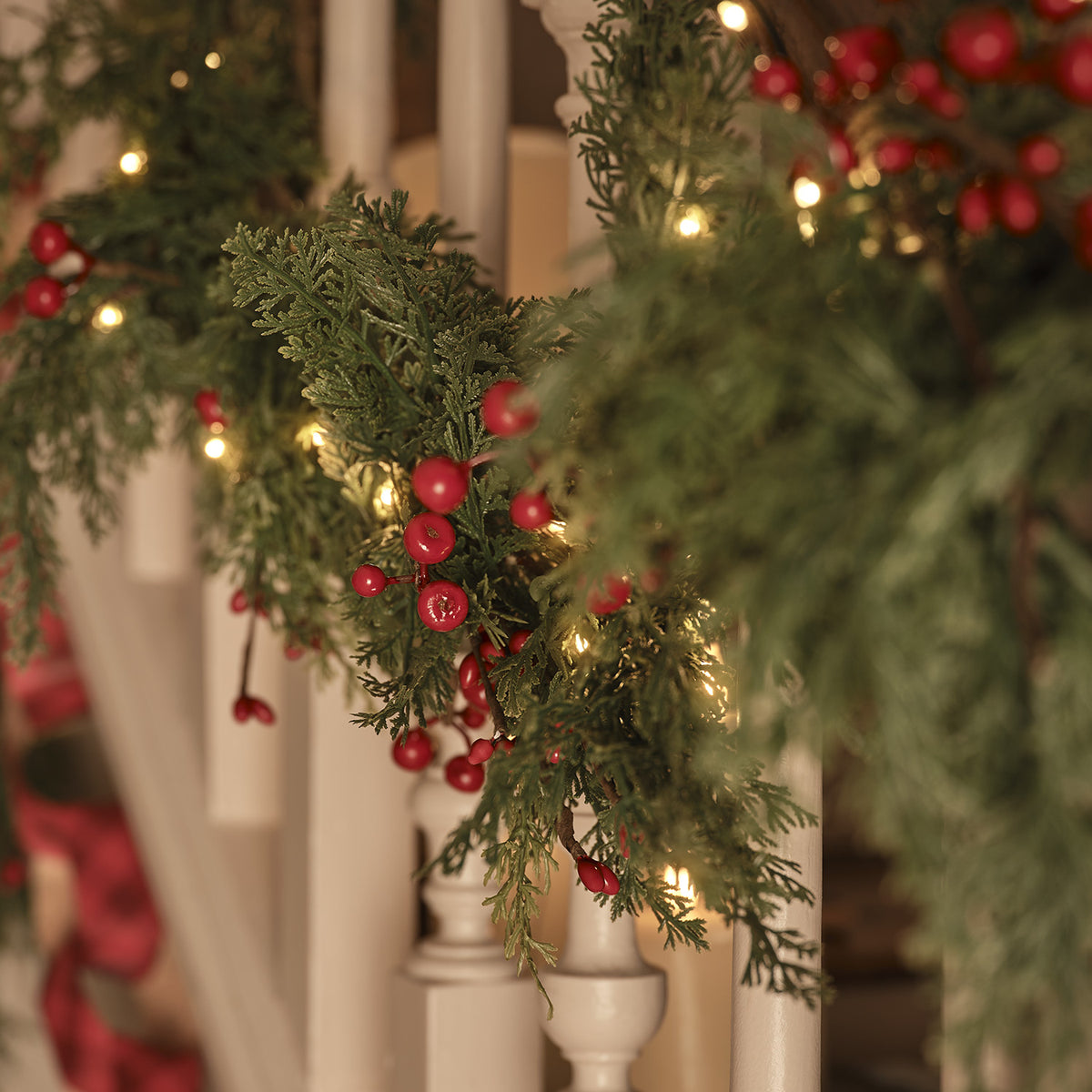 Weihnachtsgirlande mit roten Beeren und warmweißen LED-Lichtern an weißem Treppengeländer