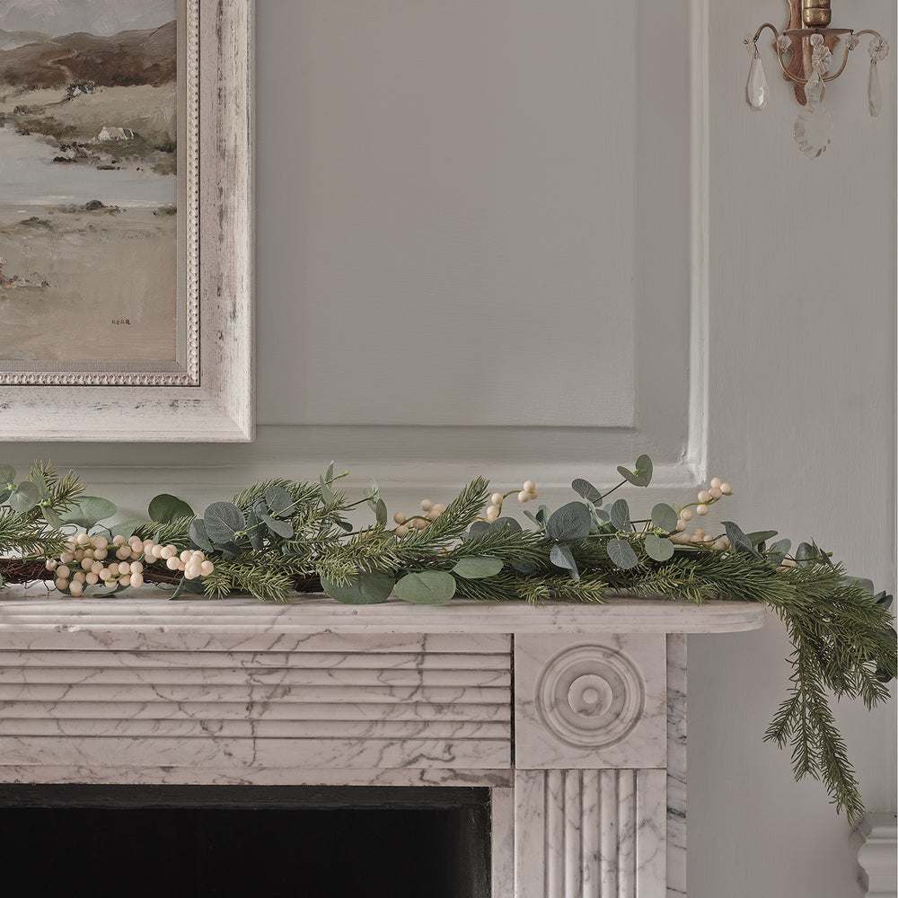 Weihnachtsgirlande mit Eukalyptusblättern und weißen Beeren auf Marmor-Kaminsims