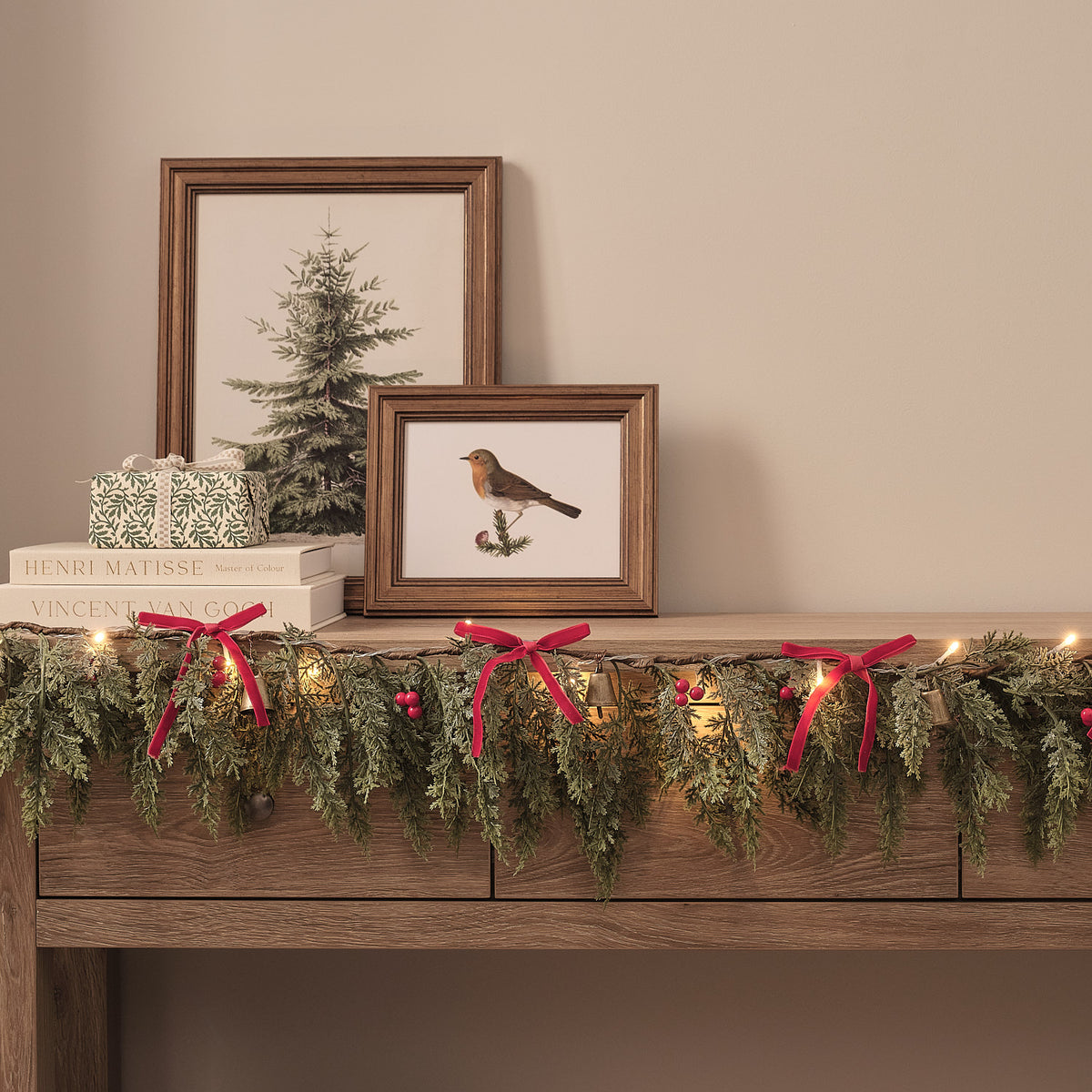 Nahaufnahme der LED-Weihnachtsgirlande mit roten Samtschleifen, Beeren und Glocken auf einer Kommode