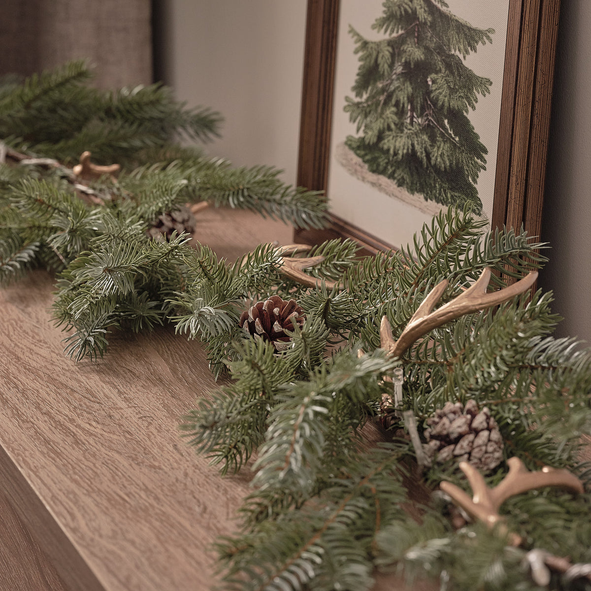 Nahaufnahme der beleuchteten Weihnachtsgirlande mit Geweih und Tannenzapfen auf Holzfläche