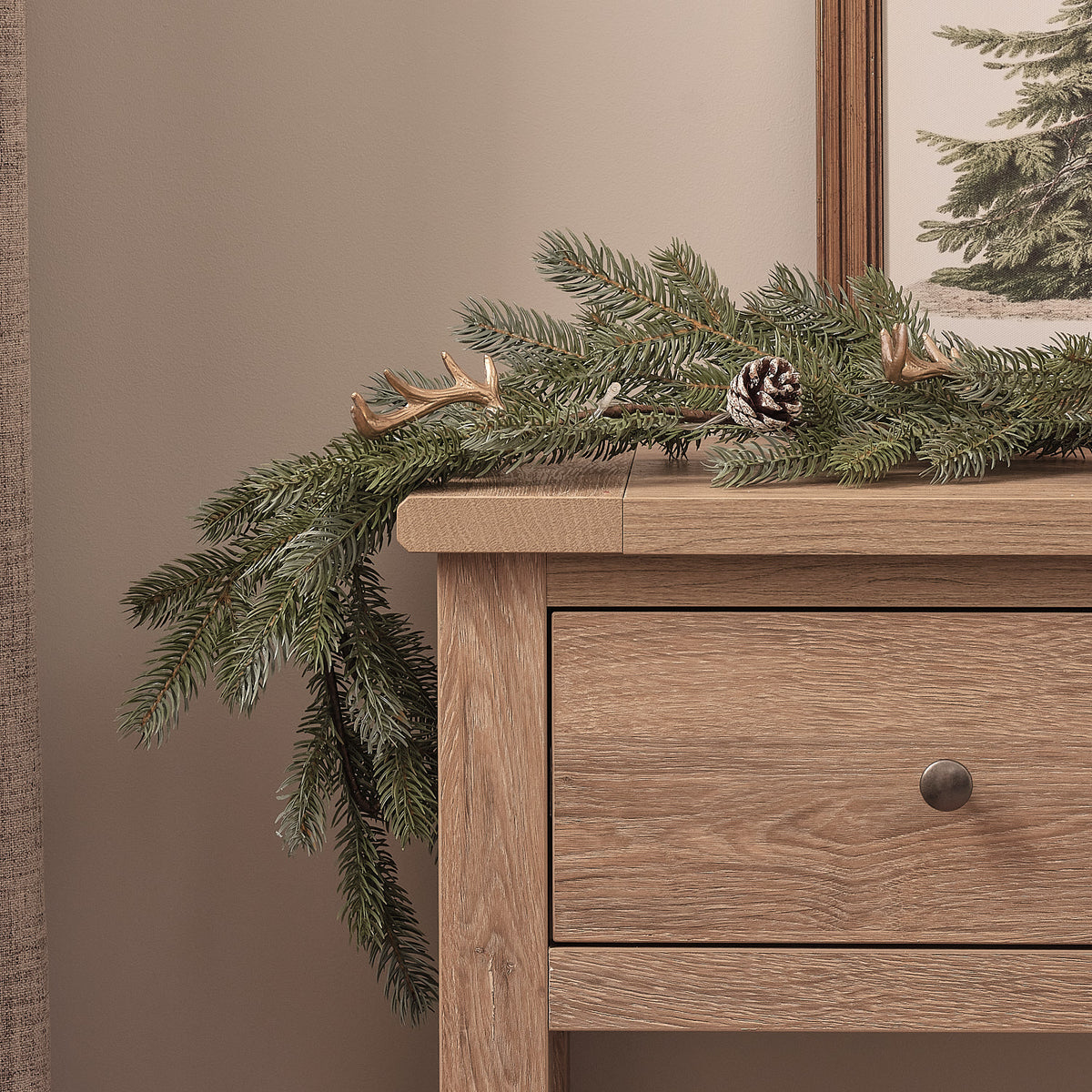 Weihnachtsgirlande mit warmweißen LEDs, Geweih und Tannenzapfen auf Holzkommode vor grauer Wand