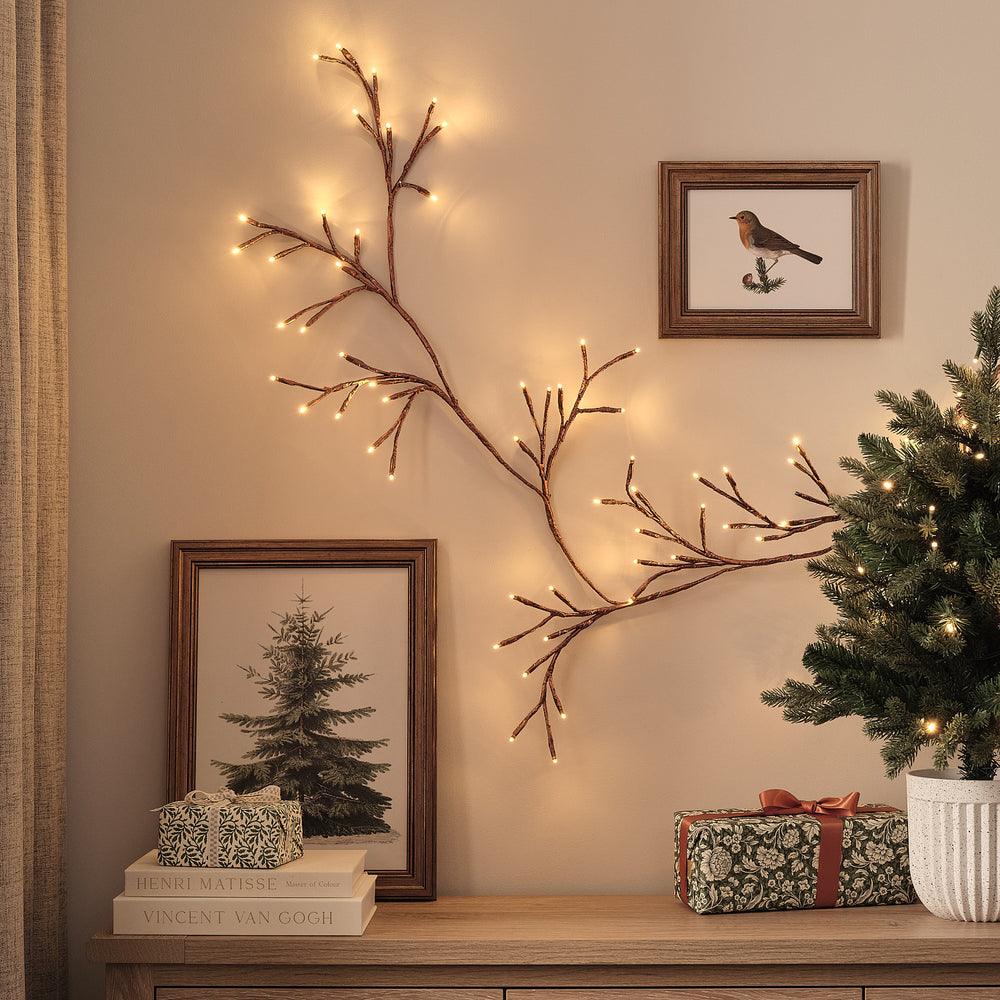 Bronzefarbene LED-Zweiggirlande mit warmweißen Lichtern an Wand über Kommode