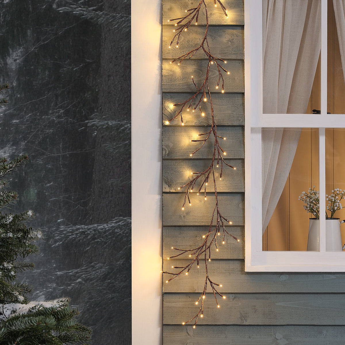 LED-Zweiggirlande außen mit warmweißen LEDs an Holzfassade neben Fenster