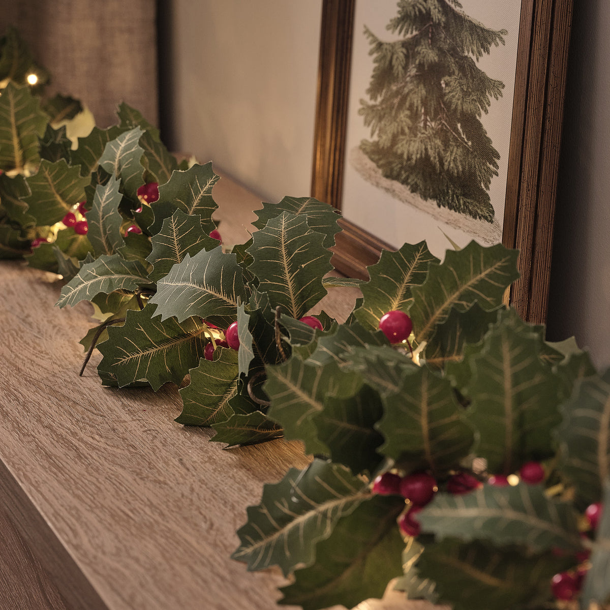 Detailaufnahme beleuchtete Weihnachtsgirlande mit Stechpalmenblättern und roten Beeren auf Sideboard