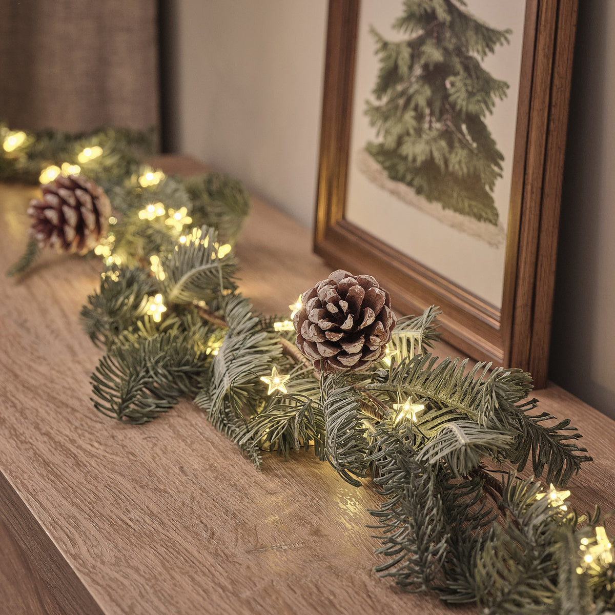 Beleuchtete Girlande mit Zapfen und warmweißen LEDs auf Holzfläche