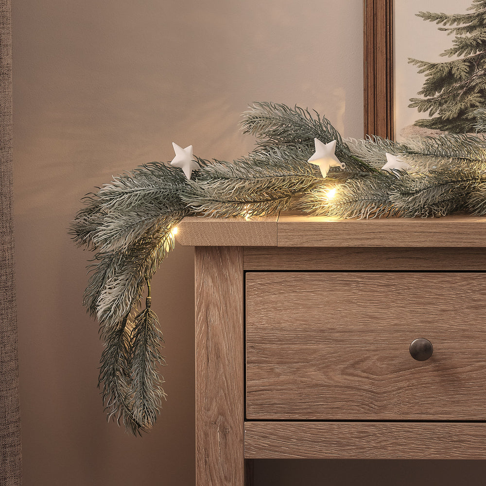 LED-Tannengirlande mit weißen Sternen dekorativ auf einem Holztisch drapiert