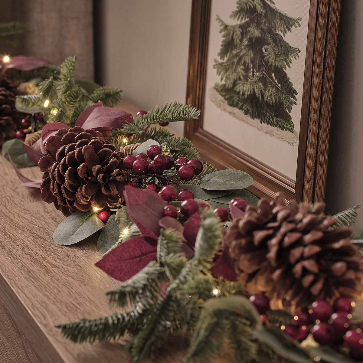 Nahaufnahme der beleuchteten Weihnachtsgirlande mit Tannenzapfen und roten Beeren auf Holzkommode