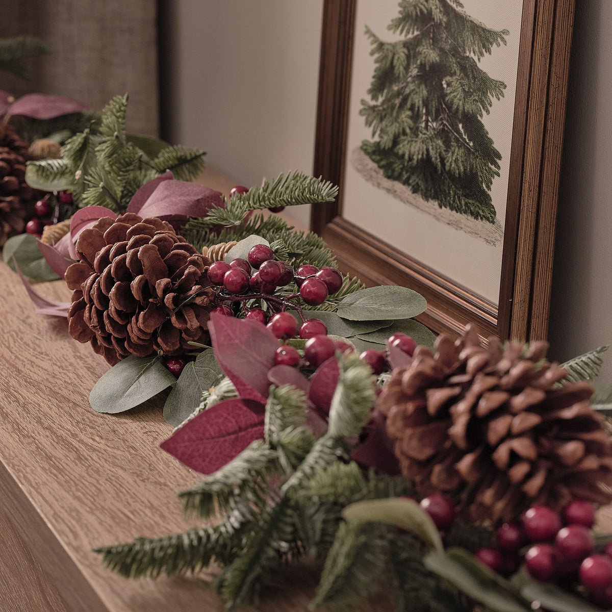 Nahaufnahme der Weihnachtsgirlande mit Tannenzapfen, roten Beeren und warmweißen LEDs neben einem gerahmten Bild