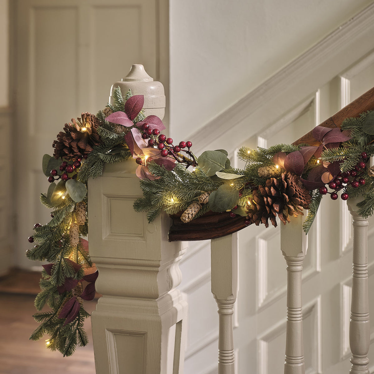 Weihnachtsgirlande mit Tannenzapfen, roten Beeren und warmweißen LEDs an Treppengeländer