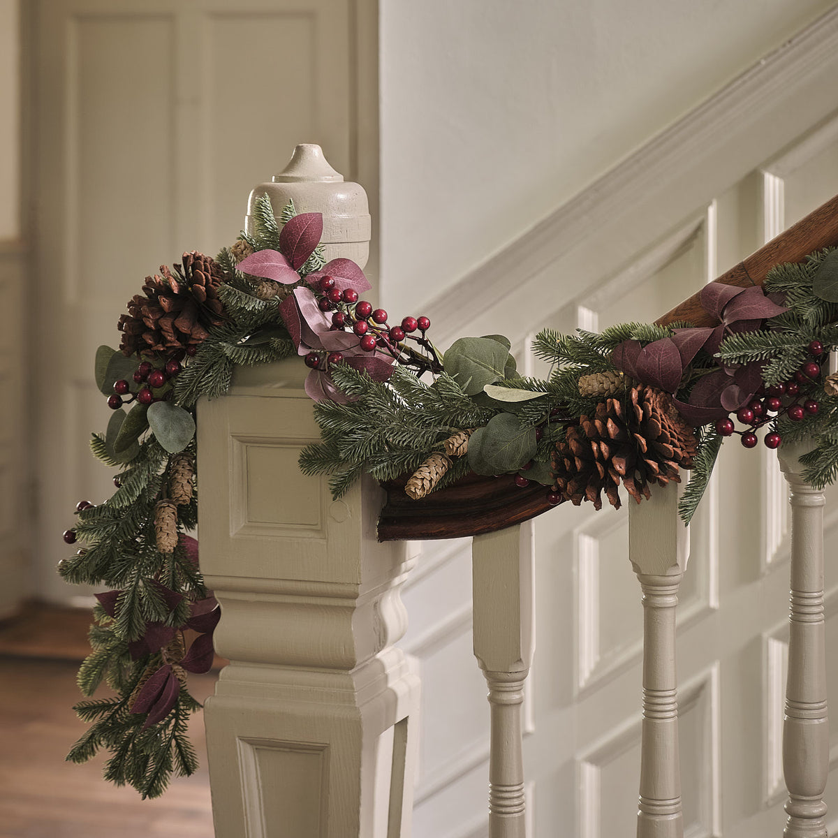 Nahaufnahme der Weihnachtsgirlande mit Tannenzapfen, roten Beeren und warmweißen LEDs neben einem gerahmten Bild