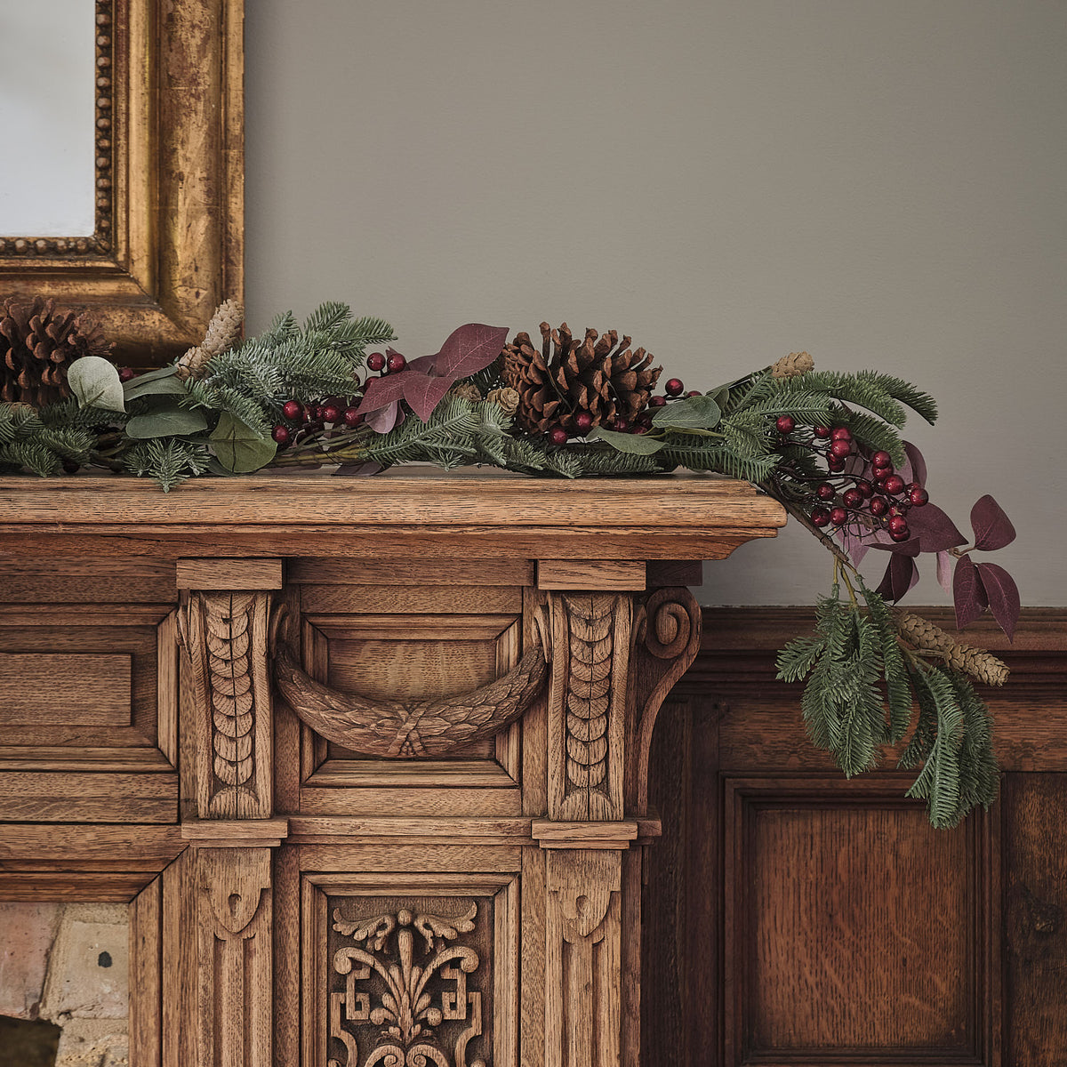 Weihnachtsgirlande mit Tannenzapfen und roten Beeren auf antikem Holzsideboard mit warmweißen LEDs