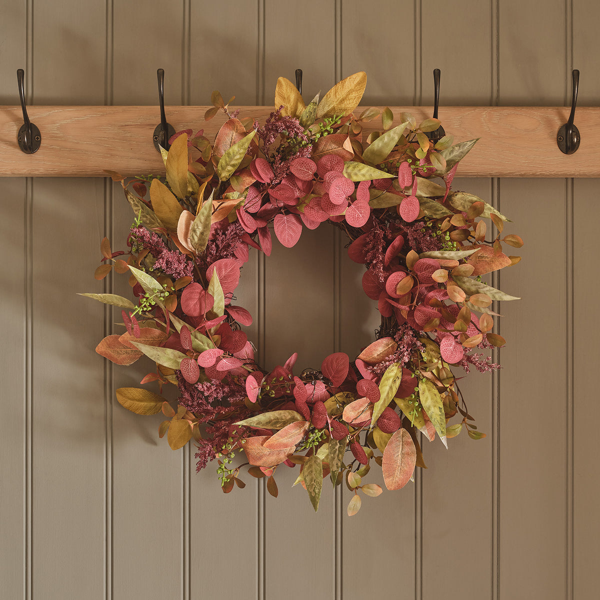 Herbstkranz mit roten und gelben Kunstblättern ohne Beleuchtung an Holzwand