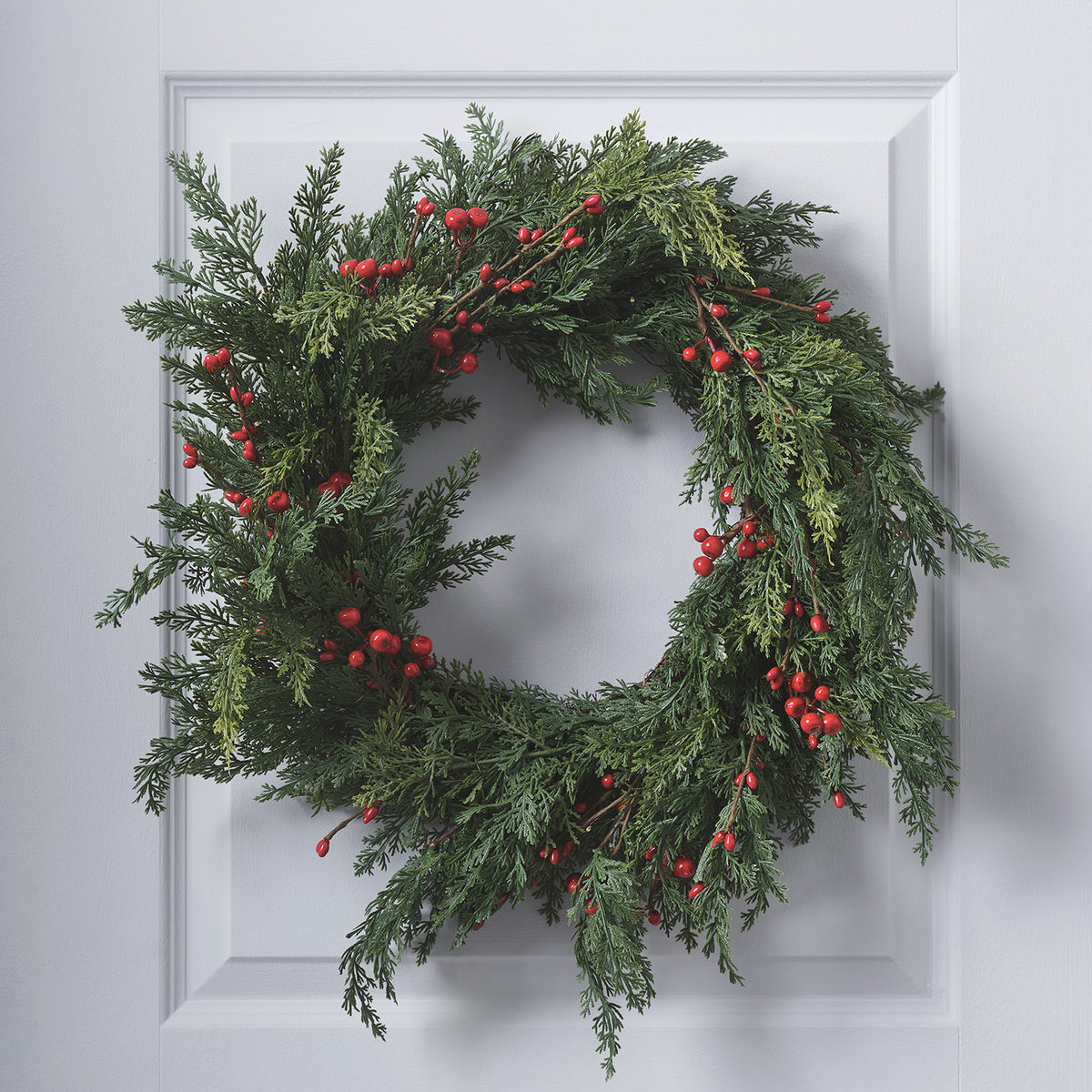 Weihnachtskranz mit roten Beeren ohne Beleuchtung an weißer Tür