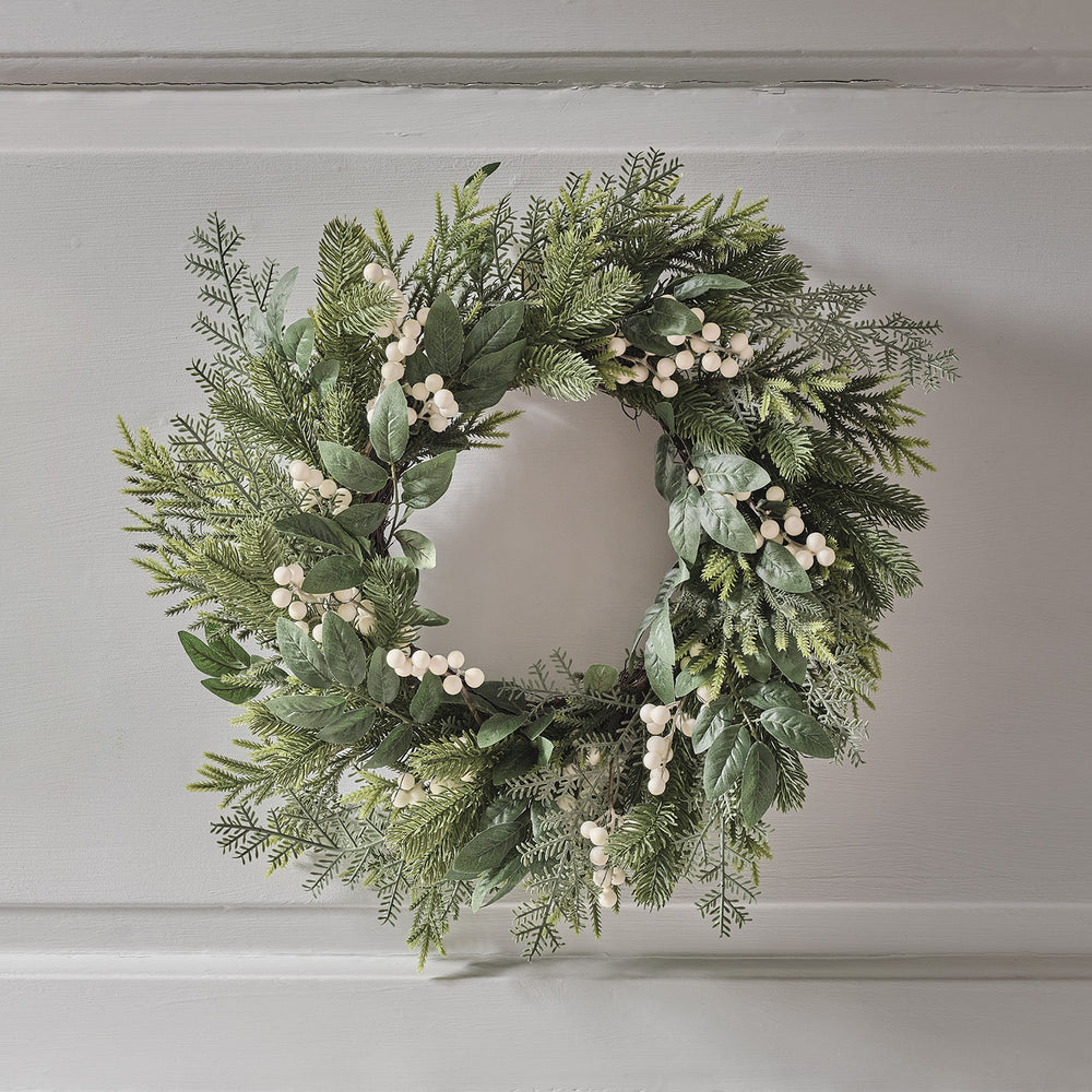Weihnachtskranz mit grünen Zweigen und weißen Beeren ohne Beleuchtung an weißer Wand