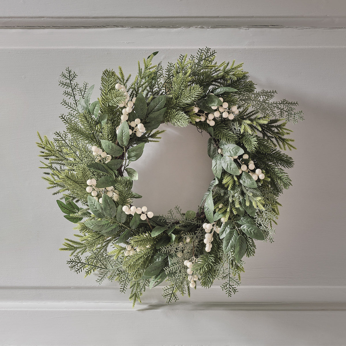 Weihnachtskranz mit grünen Zweigen und weißen Beeren ohne Beleuchtung an weißer Wand