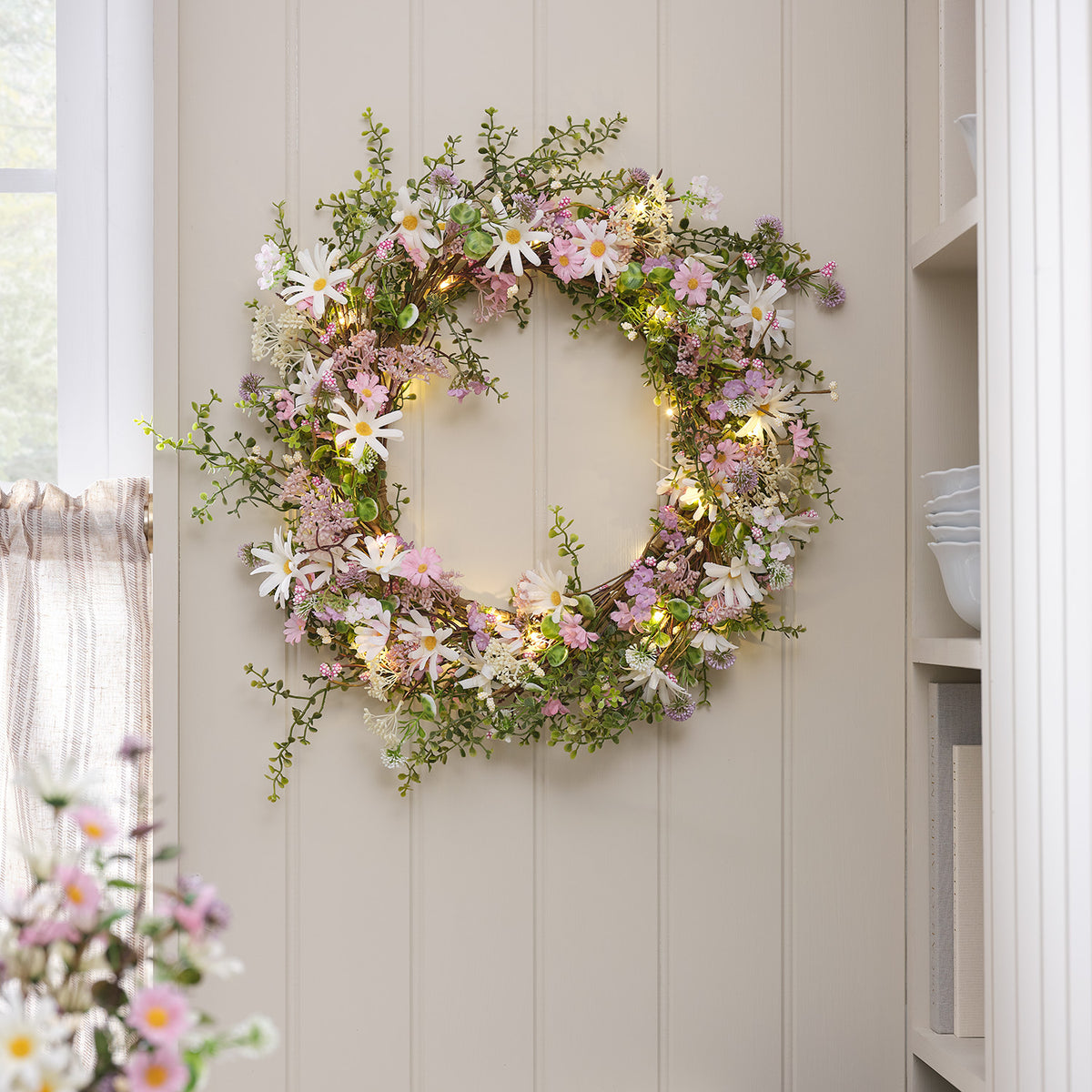 Beleuchteter Frühlingskranz mit Gänseblümchen an heller Wand im Raum