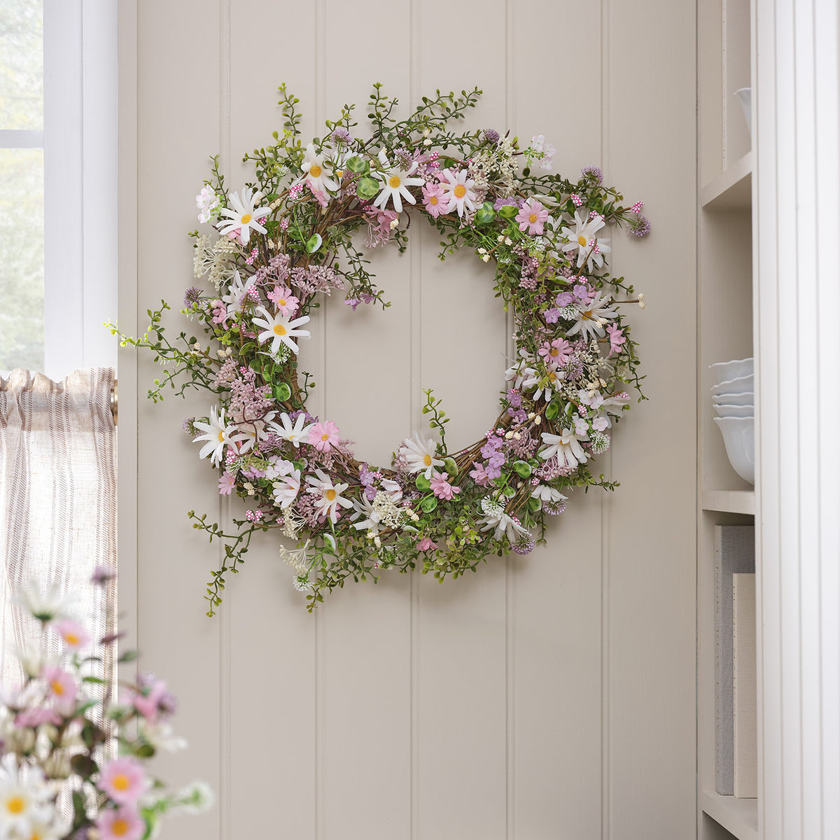 Frühlingskranz mit rosa und weißen Gänseblümchen an heller Wand hängend