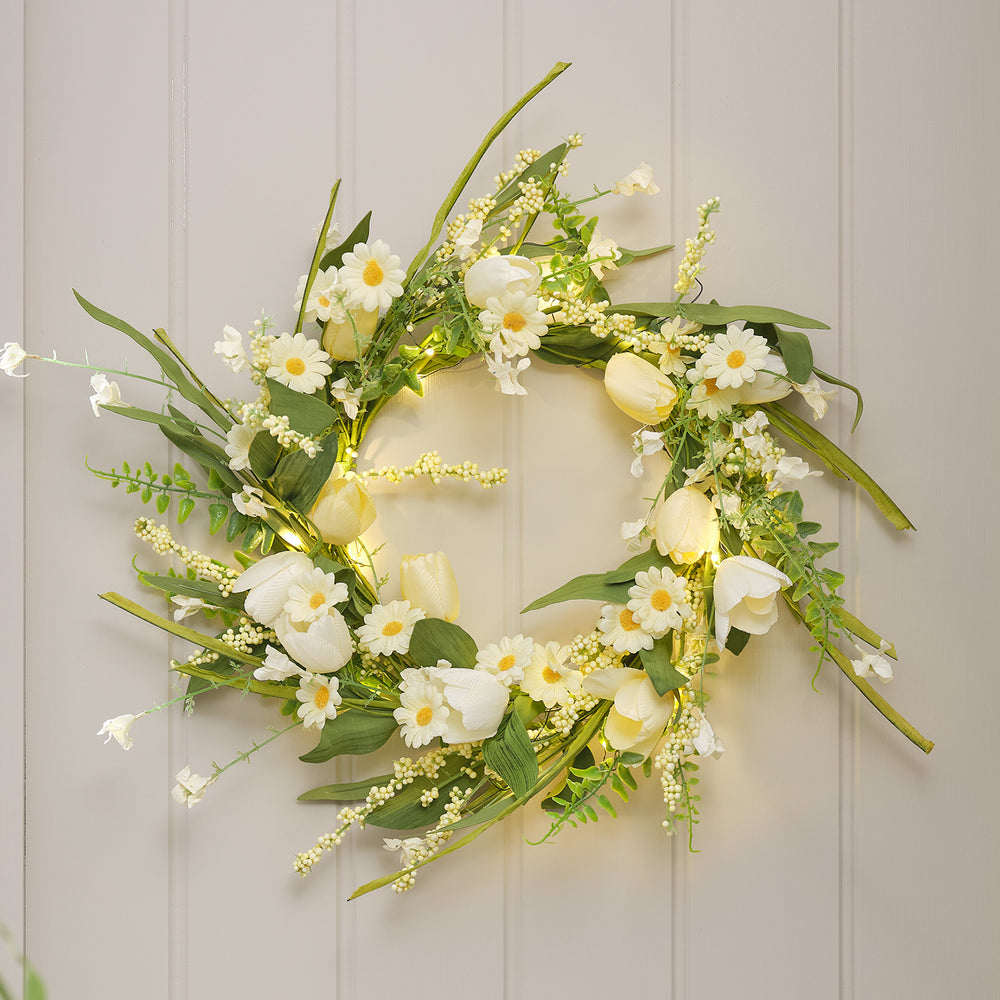 LED-Frühlingskranz mit buttergelben Tulpen, weißen Gänseblümchen und grünen Blättern an Wand