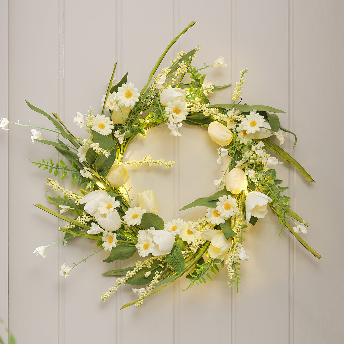 LED-Frühlingskranz mit buttergelben Tulpen, weißen Gänseblümchen und grünen Blättern an Wand