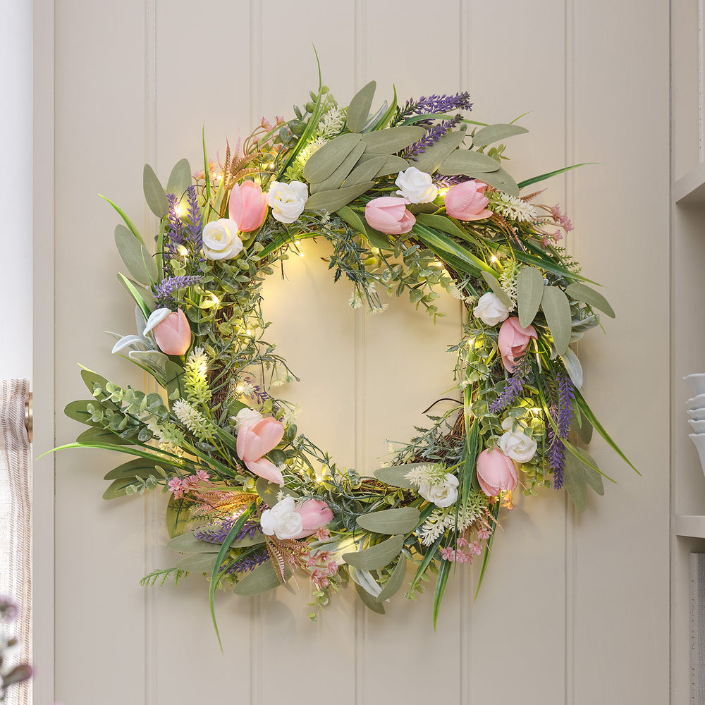 LED-Tulpenkranz mit rosa Tulpen, Lavendel, weißen Rosen und warmweißen Mikro-LEDs an einer hellen Tür