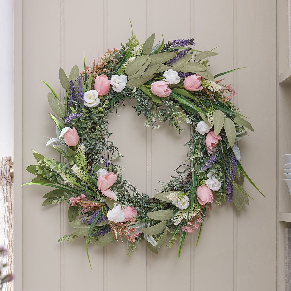 Unbeleuchteter Tulpenkranz mit rosa Tulpen, Lavendel und weißen Rosen an einer hellen Holzwand