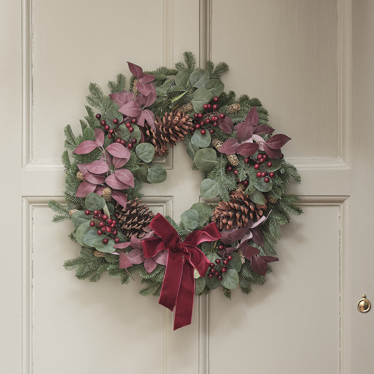 Weihnachtskranz mit roten und grünen Blättern, Tannenzapfen und roter Schleife an Tür