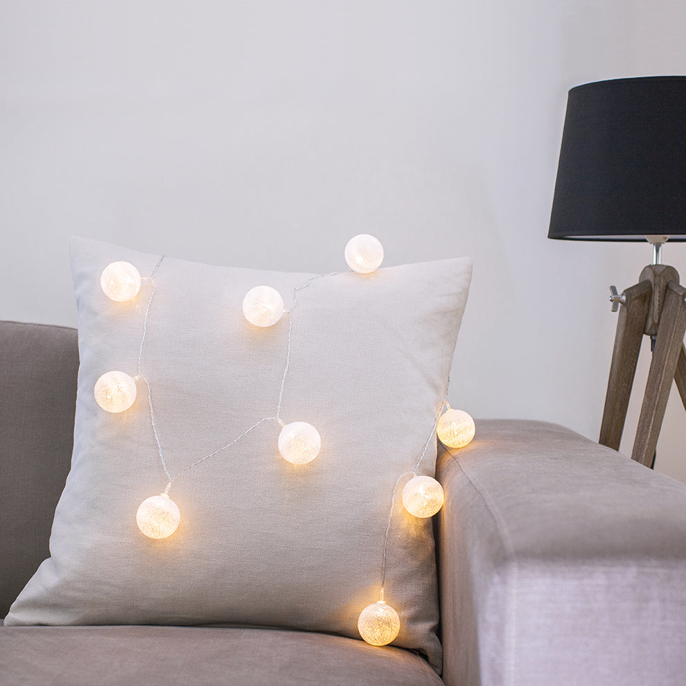 Lichterkette mit warmweißen Baumwollkugeln dekorativ auf hellem Kissen auf grauem Sofa