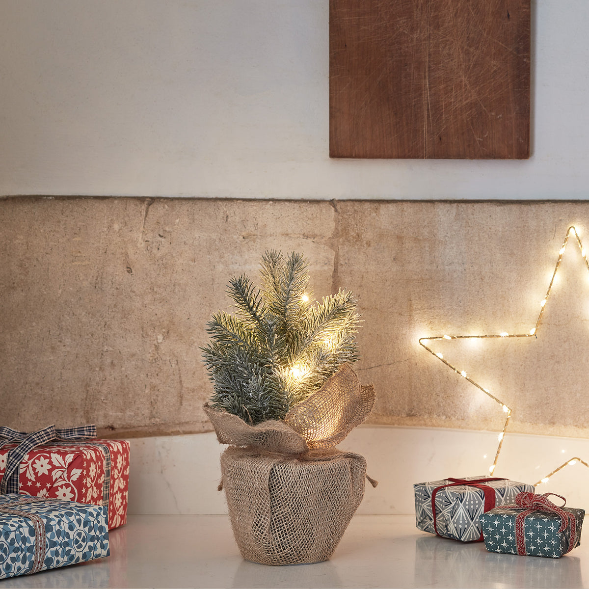 Kleiner LED Weihnachtsbaum mit Kunstschnee in Jutebeutel auf weißer Oberfläche mit Geschenken