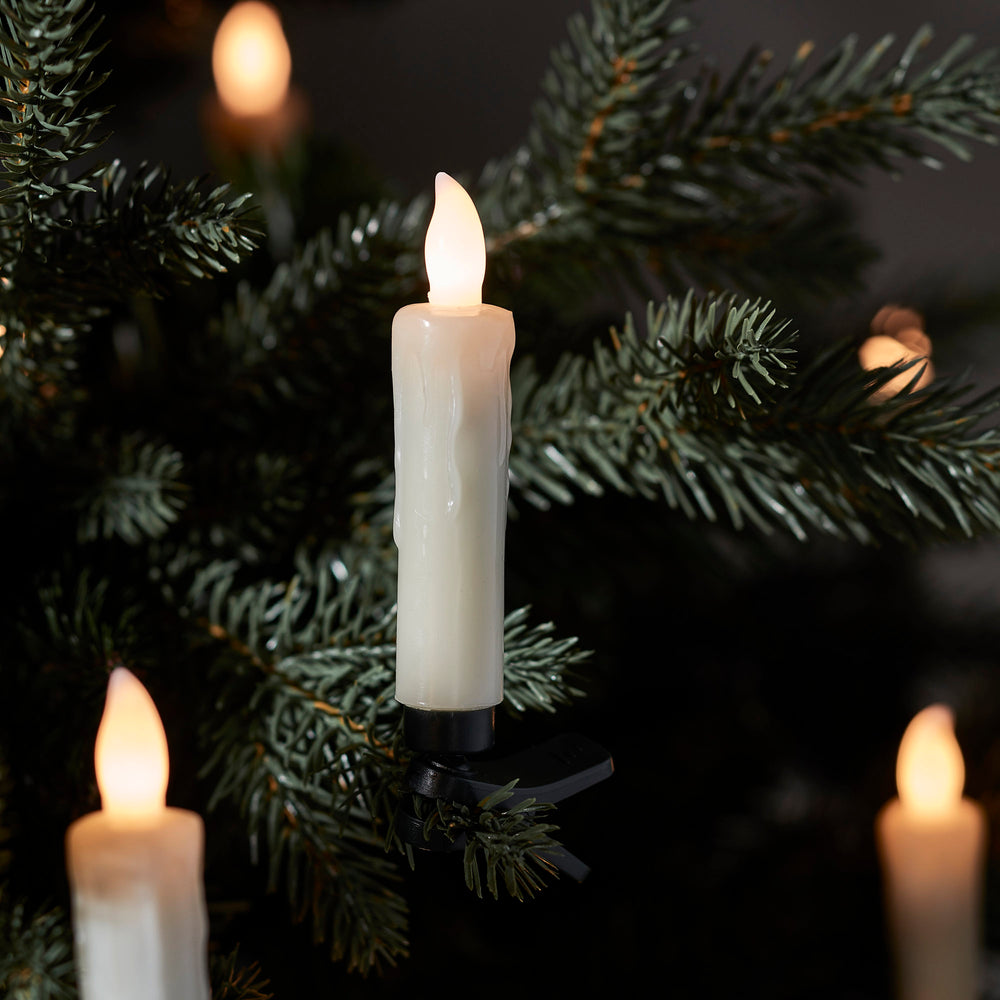 Nahaufnahme einer elfenbeinfarbenen LED-Weihnachtsbaumkerze mit warmweißem Licht auf Tannenzweig
