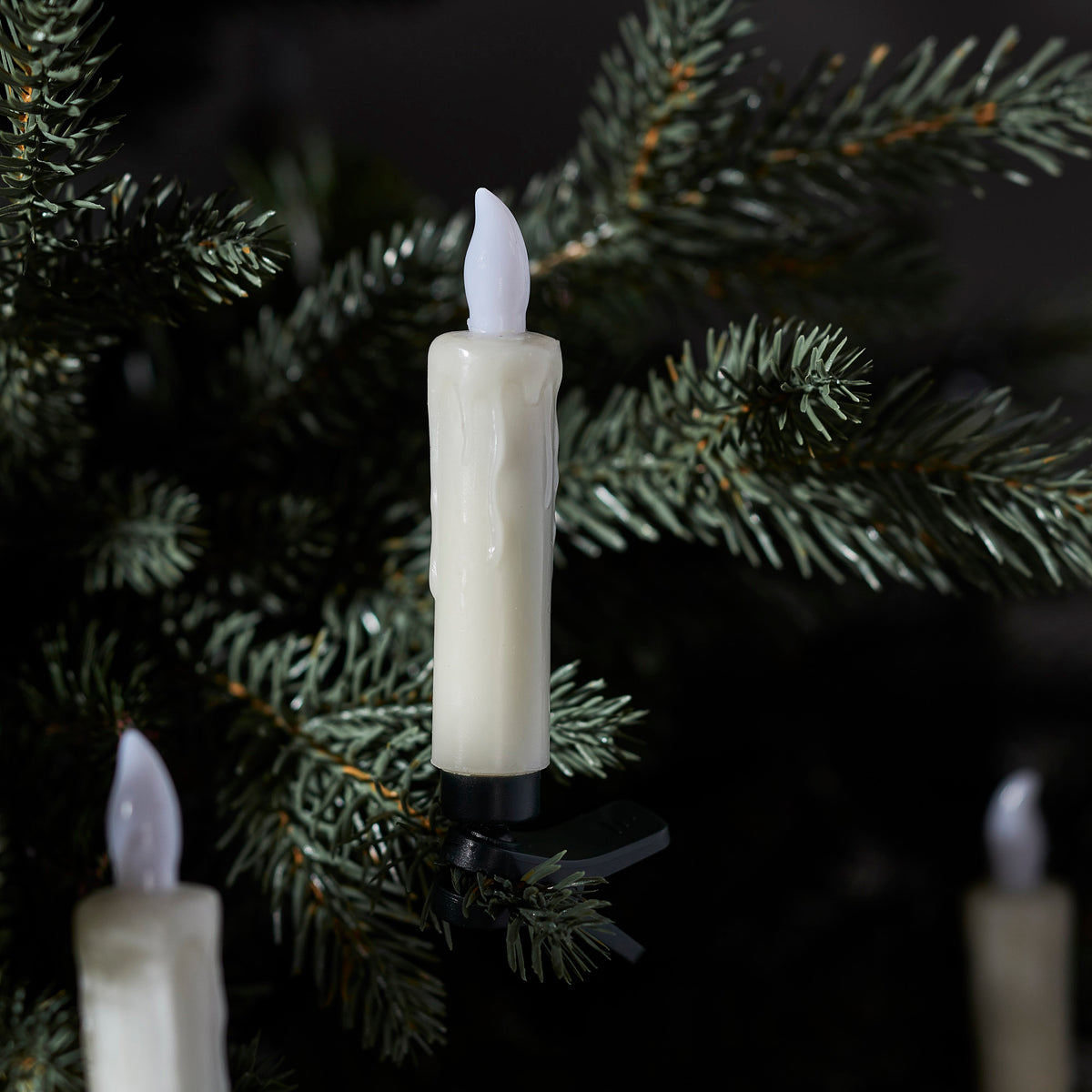 Hand hält Fernbedienung zur Steuerung der warmweißen LED-Weihnachtsbaumkerze am Baum