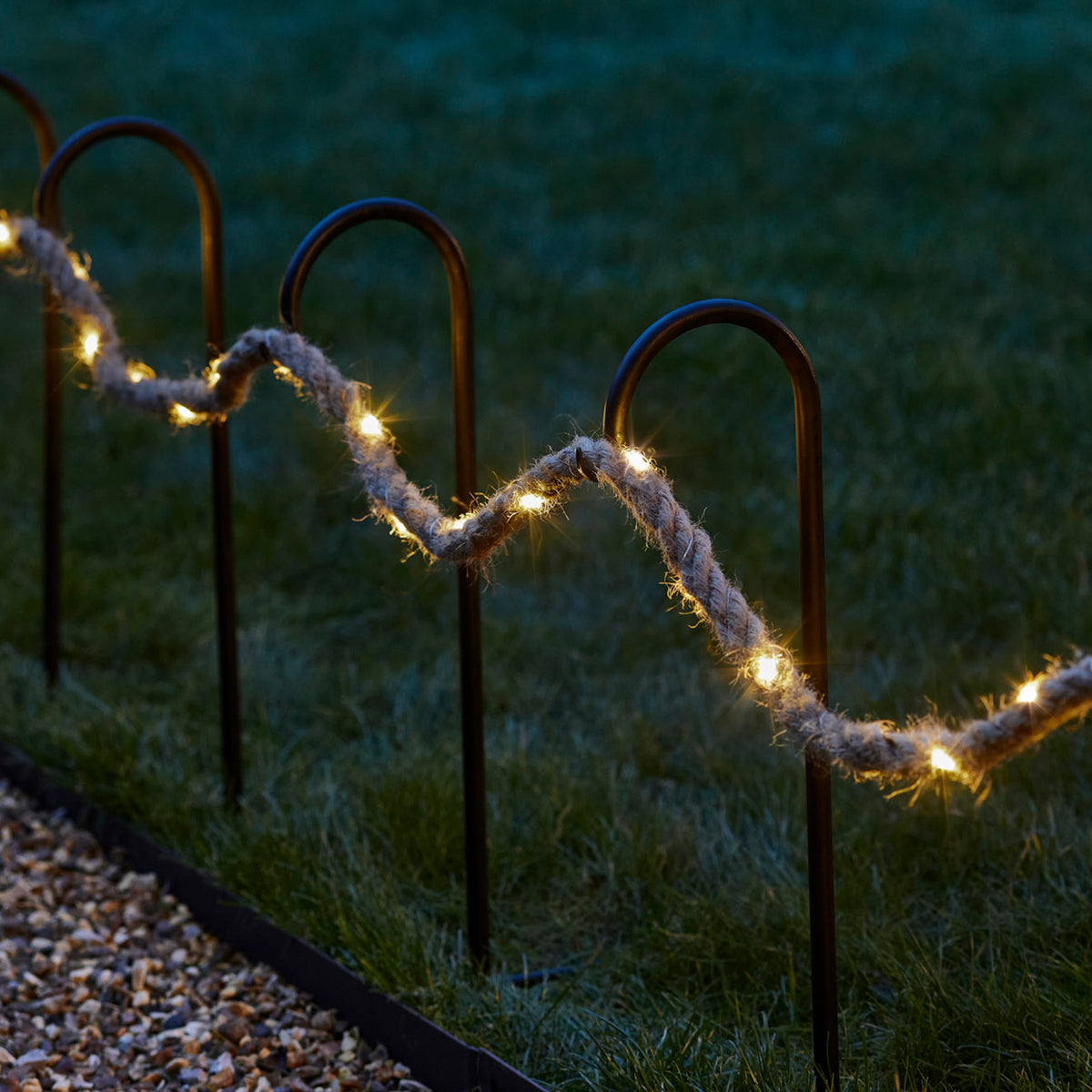 Beleuchtetes Seil mit warmweißen Micro LEDs als Lichterkette im Garten an Metallstäben befestigt
